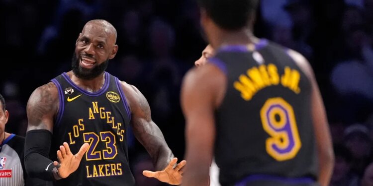LeBron James in a Lakers uniform with his hands up, facing Bronny James, whose back is to the camera.