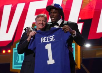 NFL Commissioner Roger Goodell and Arvell Reese holding up a New York Giants jersey with "Reese" and the number "1" on it.
