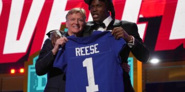 NFL Commissioner Roger Goodell and Arvell Reese holding up a New York Giants jersey with "Reese" and the number "1" on it.