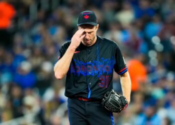 Toronto Blue Jays pitcher Max Scherzer in a black jersey and cap, touching his head.