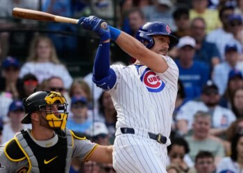 Michael Conforto in a white Cubs uniform with blue pinstripes hitting a baseball.