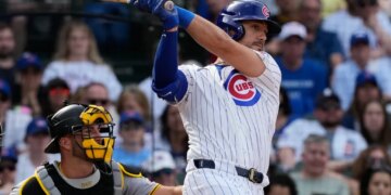 Michael Conforto in a white Cubs uniform with blue pinstripes hitting a baseball.