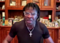 Deion Sanders wearing glasses and a black shirt with a silver cross necklace.