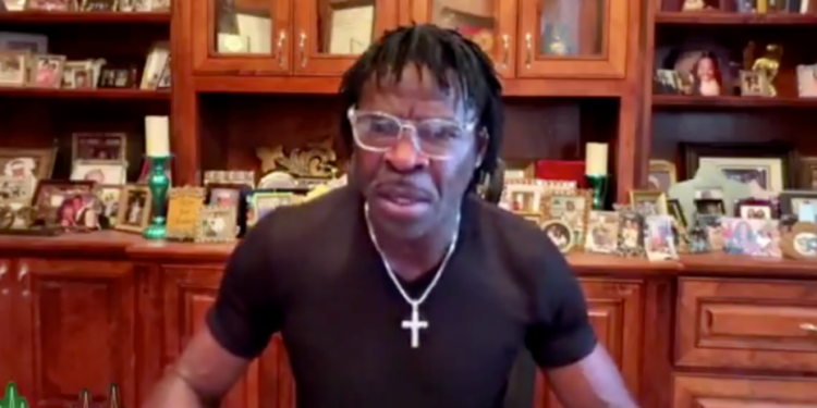 Deion Sanders wearing glasses and a black shirt with a silver cross necklace.