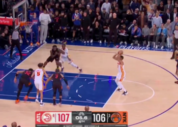 A basketball player in a white and orange uniform shoots a jump shot with 5.6 seconds left in the 4th quarter, Hawks leading Knicks 107-106.