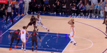 A basketball player in a white and orange uniform shoots a jump shot with 5.6 seconds left in the 4th quarter, Hawks leading Knicks 107-106.