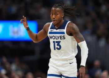 Ayo Dosunmu in a white "Wolves 13" jersey with his right arm raised and dreadlocks flowing to the right.