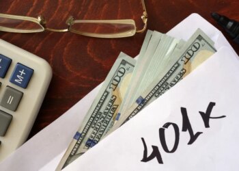 An envelope with "401k" written on it, filled with US dollar bills, next to a calculator and eyeglasses.