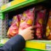 A person's hand reaching for a pink bag of Lay's potato chips on a store shelf.