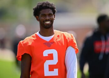 Shedeur Sanders smiles while wearing an orange practice jersey with the number 2.