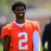 Shedeur Sanders smiles while wearing an orange practice jersey with the number 2.