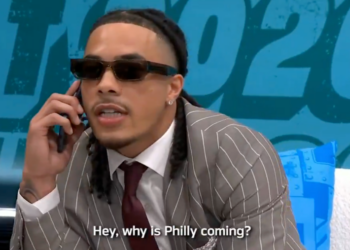 A man in a striped suit and sunglasses talks on the phone, saying "Hey, why is Philly coming?"