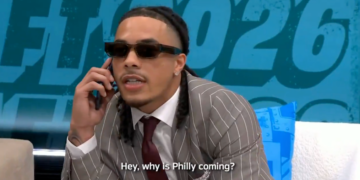 A man in a striped suit and sunglasses talks on the phone, saying "Hey, why is Philly coming?"