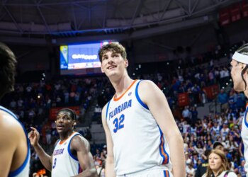Olivier Rioux in a Florida Gators basketball uniform smiling on the court with teammates.