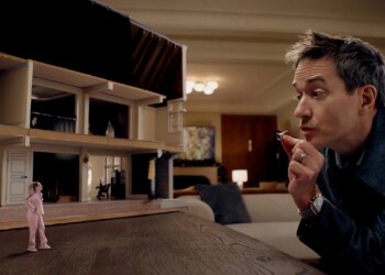 A tiny woman standing next to a bisected dollhouse as she has an argument with a gigantic man the size of a mountain.