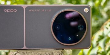 Photo of Oppo Find X9 Ultra resting horizontally on a wooden post in front of green plants, showing the rear cameras