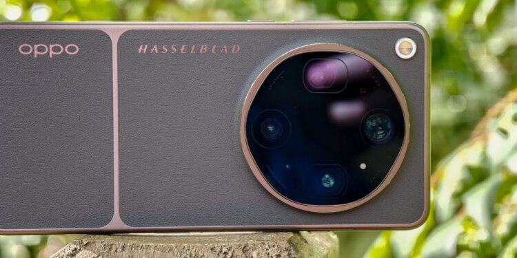 Photo of Oppo Find X9 Ultra resting horizontally on a wooden post in front of green plants, showing the rear cameras