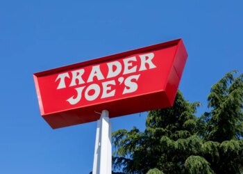 Red Trader Joe's sign against a blue sky, with pine trees visible.