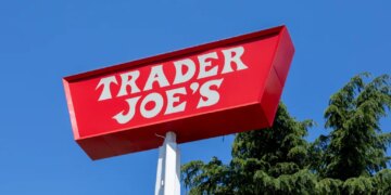 Red Trader Joe's sign against a blue sky, with pine trees visible.