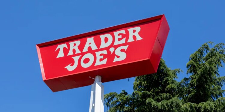 Red Trader Joe's sign against a blue sky, with pine trees visible.