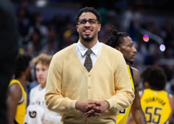 Indiana Pacers guard Tyrese Haliburton smiling while wearing a yellow cardigan, white collared shirt, and patterned tie.