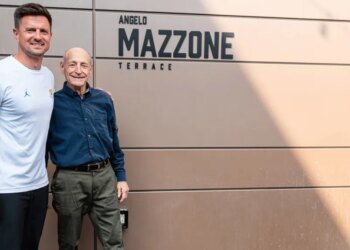 Two men smiling in front of a wall with "Angelo Mazzone Terrace" written on it.