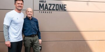 Two men smiling in front of a wall with "Angelo Mazzone Terrace" written on it.