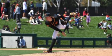 A baseball pitcher in a black and orange uniform mid-delivery.