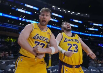 Two Lakers fans, Tom Biddle and Mantis Taylor, wearing Luka Doncic and Lebron James jerseys respectively, cheer from the stands.