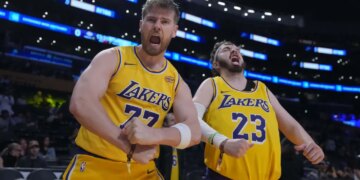 Two Lakers fans, Tom Biddle and Mantis Taylor, wearing Luka Doncic and Lebron James jerseys respectively, cheer from the stands.