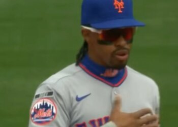Baseball player in a New York Mets uniform with sunglasses and a hat with the team's logo.
