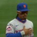 Baseball player in a New York Mets uniform with sunglasses and a hat with the team's logo.