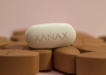 A white oblong pill with "XANAX" imprinted on it sits on a bed of brown pills.