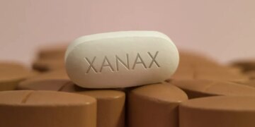 A white oblong pill with "XANAX" imprinted on it sits on a bed of brown pills.