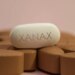 A white oblong pill with "XANAX" imprinted on it sits on a bed of brown pills.