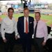 Three men posing for a photo in a broadcast booth overlooking Yankee Stadium.