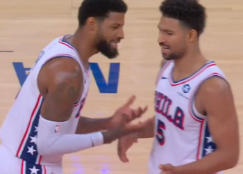 Two basketball players in white jerseys with red and blue accents, facing each other on the court.