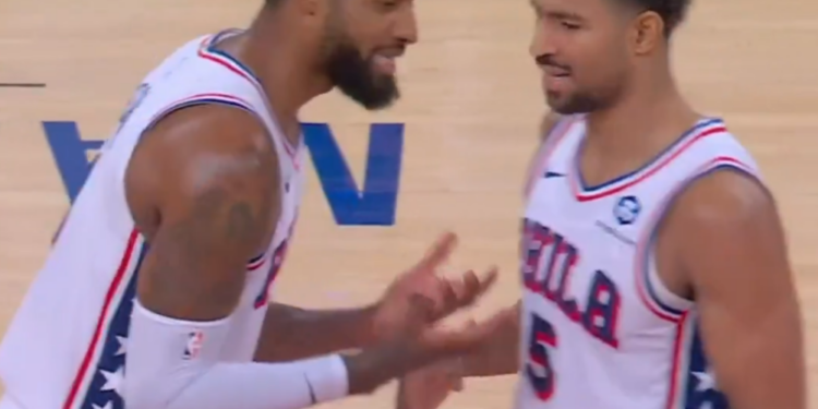 Two basketball players in white jerseys with red and blue accents, facing each other on the court.