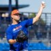 A baseball player in a blue Mets shirt and orange hat throwing a baseball during spring training.