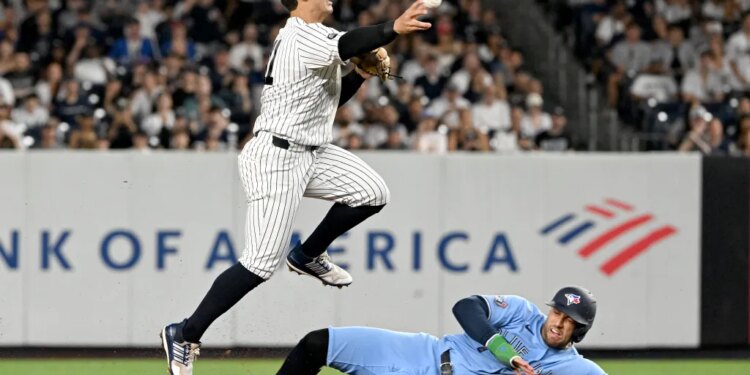Yankees shortstop Anthony Volpe jumps over Blue Jays designated hitter George Springer during a double play.