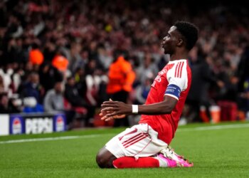 Arsenal player Bukayo Saka celebrates a goal on one knee.