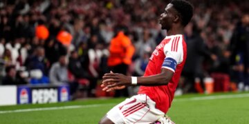 Arsenal player Bukayo Saka celebrates a goal on one knee.