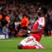 Arsenal player Bukayo Saka celebrates a goal on one knee.