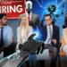 illustration four people sitting holding paper wit a red and white now hiring sign behind them and robots all around them