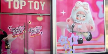 Storefront of the new Top Toy store in Times Square, with pink signs reading "TOP TOY" and "Coming Soon TRENDY TOY" on the left doors, and an illustration of a large cartoon doll in a fluffy pink outfit on the right window.