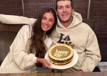A couple smiles while holding a "happy 23rd" birthday cake.