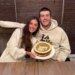 A couple smiles while holding a "happy 23rd" birthday cake.