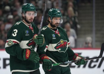 Minnesota Wild players Quinn Hughes and Ryan Hartman on the ice during an NHL playoff game.