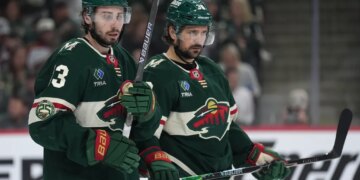 Minnesota Wild players Quinn Hughes and Ryan Hartman on the ice during an NHL playoff game.