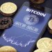 Illustration of a smartphone displaying a Bitcoin trading app with buy/sell options and a price chart, surrounded by stacks of golden Bitcoin coins.